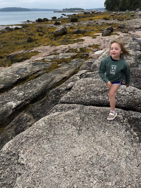 Child wearing Basil kid crew sweatshirt playing on rocky beach