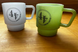 Two milk glass coffee mugs with black circle "44 North Coffee" on a wooden table, one mist blue and one jade green.