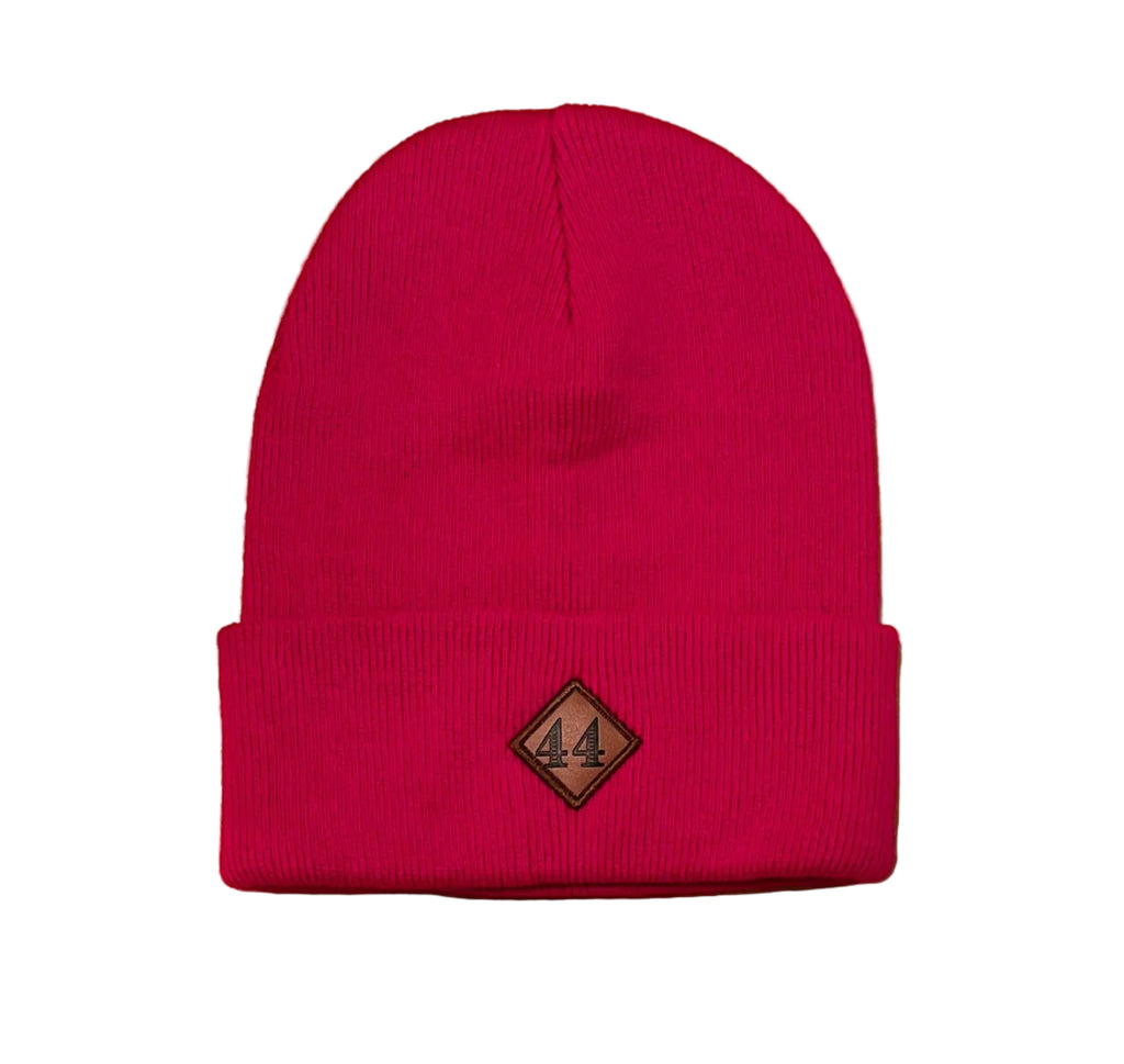 A bright pink knit beanie hat with a small diamond-shaped brown logo patch on the front cuff.