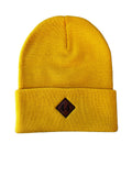 A mustard yellow knit beanie hat with a folded cuff and a small leather diamond-shaped 44 North Coffee logo patch laid flat on a white surface